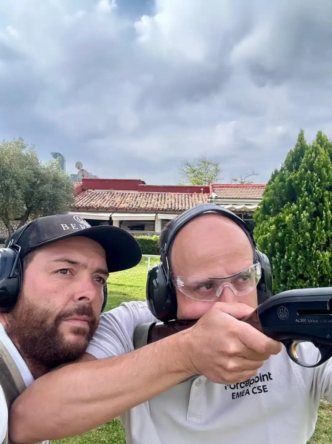 Gonzalo Gómez Arrimadas dando indicaciones técnicas a un alumno durante una clase de tiro deportivo en campo oficial, ambos con protección auditiva.