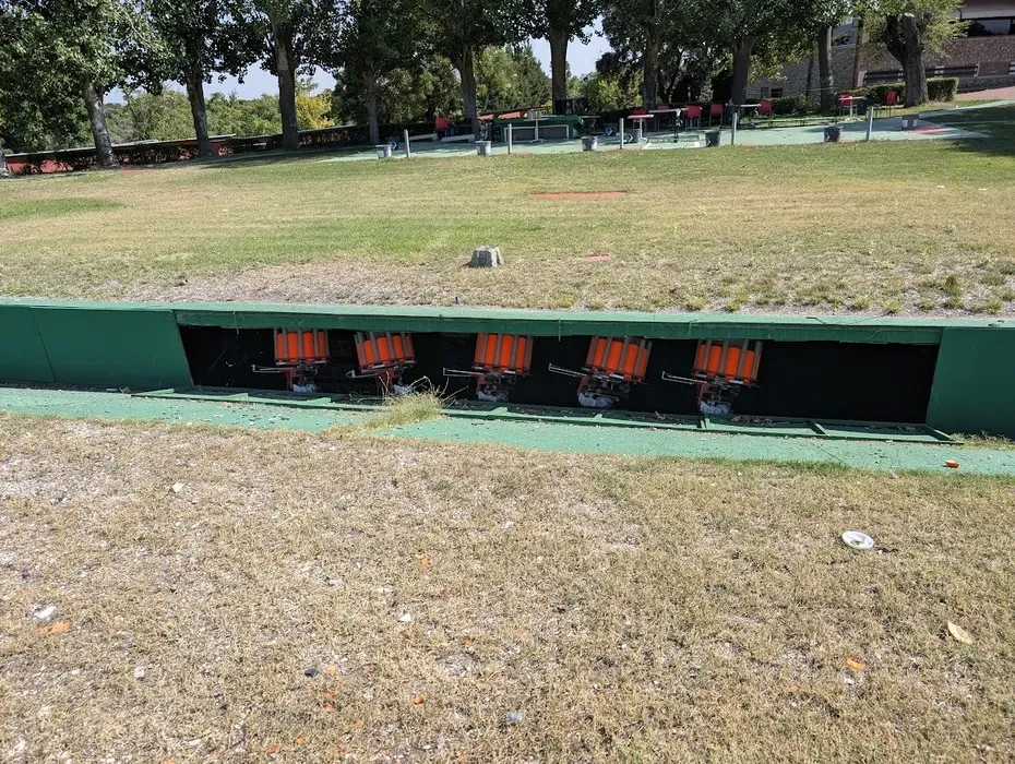 Gonzalo Gómez Arrimadas dando indicaciones técnicas a un alumno durante una clase de tiro deportivo en campo oficial, ambos con protección auditiva.
