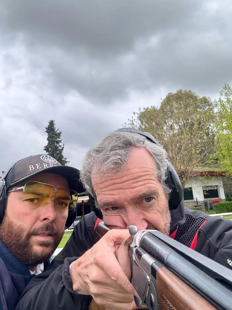 Gonzalo Gómez Arrimadas dando indicaciones técnicas a un alumno durante una clase de tiro deportivo en campo oficial, ambos con protección auditiva.